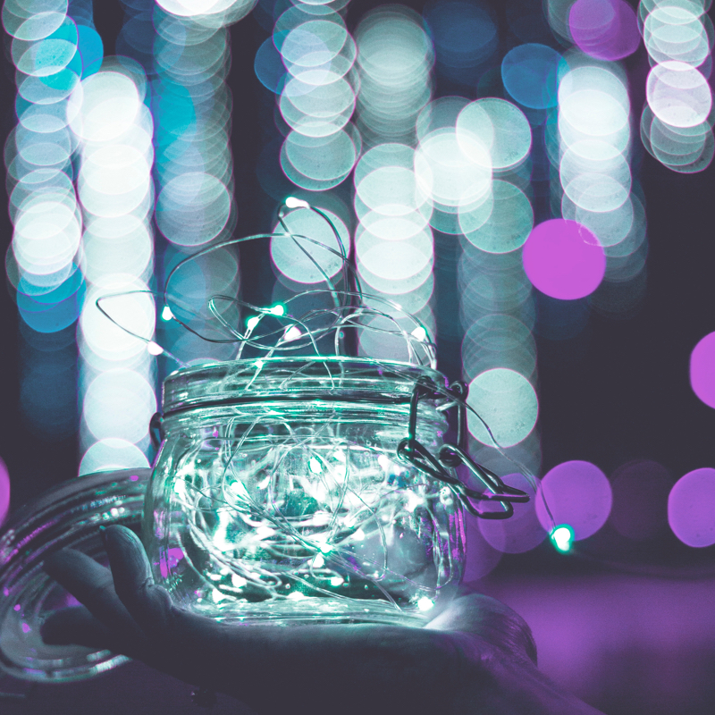 white coloured string lights in a mason jar with purple and white stringlight blurred in the background