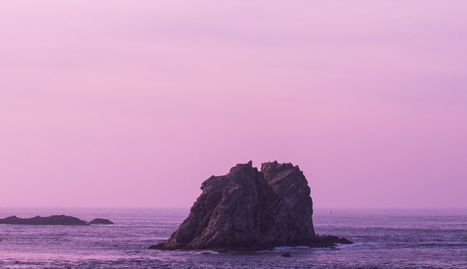 huge rock or a small island in the ocean during a sunset